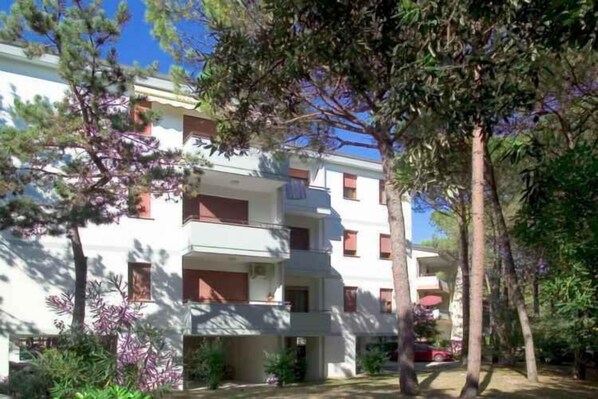 A multi-story building with balconies, surrounded by trees and greenery.