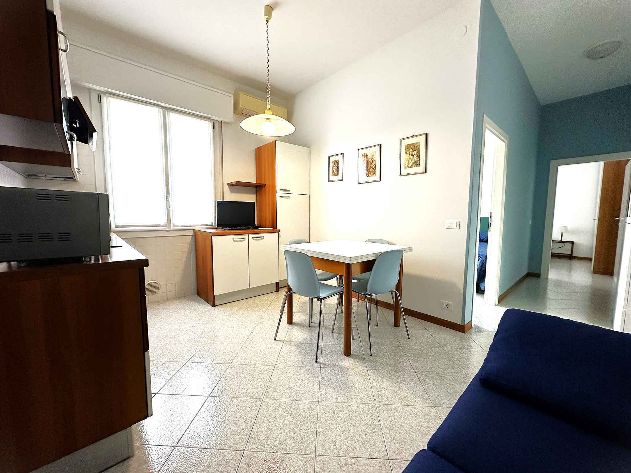 A compact kitchen with a dining area, a TV on the counter, and a blue sofa in the foreground.