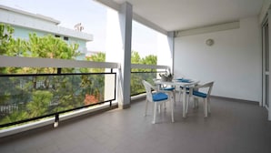 A balcony with a table and chairs, a view of greenery, and a building in the background.