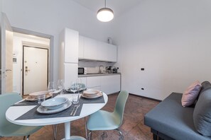A compact living space with a dining table set for four, a kitchenette, and a sofa with cushions.
