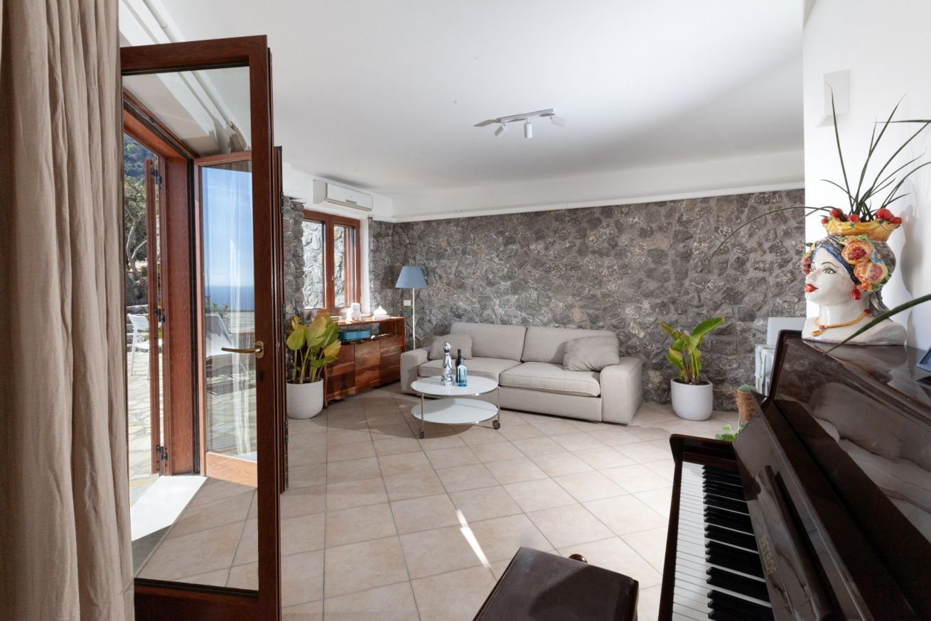 Een woonkamer met een piano, een bank, een salontafel en een stenen muur.