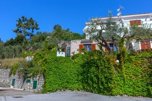 Un bâtiment situé sur une colline, avec des murs en pierre, des volets verts et un ciel d’un bleu éclatant.