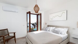 Un dormitorio con cama, una silla, una lámpara colgante, una ventana y un aire acondicionado instalado en la pared.