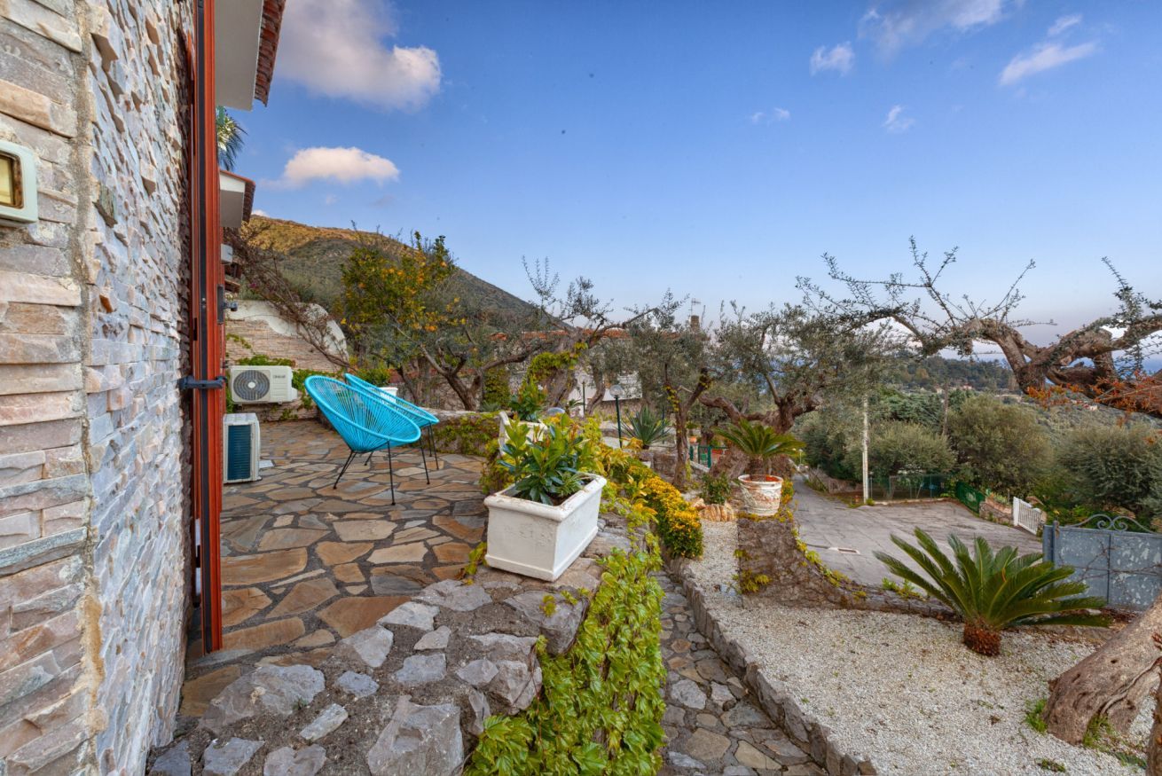 Une terrasse en pierre avec une chaise bleue, des plantes en pot et une vue sur une colline.