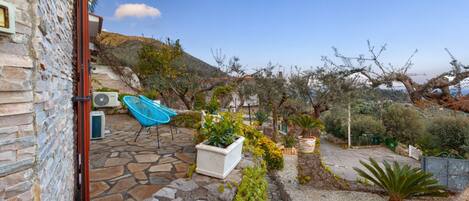 Un patio de piedra con una silla azul, plantas en macetas y vistas a una ladera.