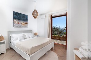 A bedroom with a bed, a painting, a hanging light fixture, and a view of the outdoors. - My Exclusive Italy - Sunlit Villa with unique pool & directly view of Nerano Bay (Nerano)