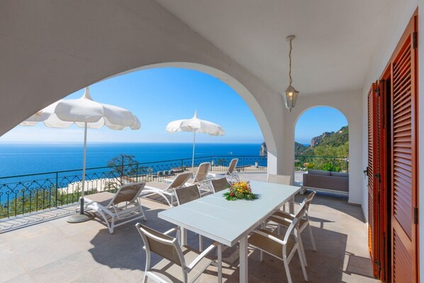 A terrace with white furniture, white umbrellas, and a view of the sea.