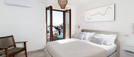 A bedroom with a bed, a chair, a hanging light fixture, a window, and a wall-mounted air conditioner.