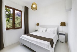 A bedroom with a bed, two bedside tables, a window with curtains, and a hanging light fixture.