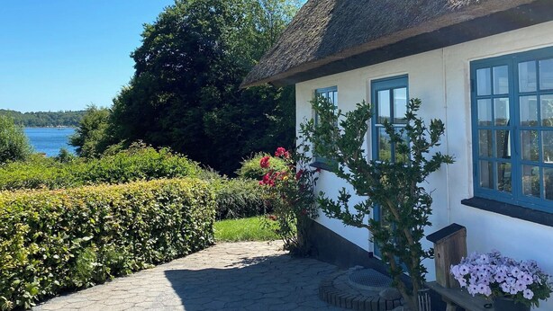 A house with a thatched roof, a garden with flowers, and a view of the water.