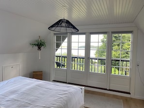 Une chambre Ă coucher avec un lit, une plante suspendue et une vue sur un balcon amĂ©nagĂ© avec du mobilier dâextĂ©rieur.