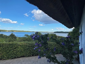 Une vue dâun lac avec un pont, entourĂ© de verdure et dâun bĂątiment au toit de chaume.