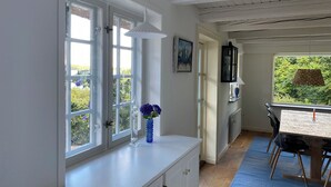 A room with a white cabinet, a blue vase with flowers, a dining table with chairs, and a window with a view of greenery.