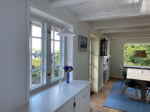 A room with a white cabinet, a blue vase with flowers, a dining table with chairs, and a window with a view of greenery. - Dream house with view of the Little Belt (Fredericia)
