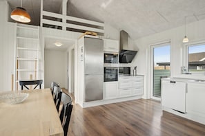 A modern kitchen with white cabinetry, a stainless steel refrigerator, and a wooden dining table with chairs.