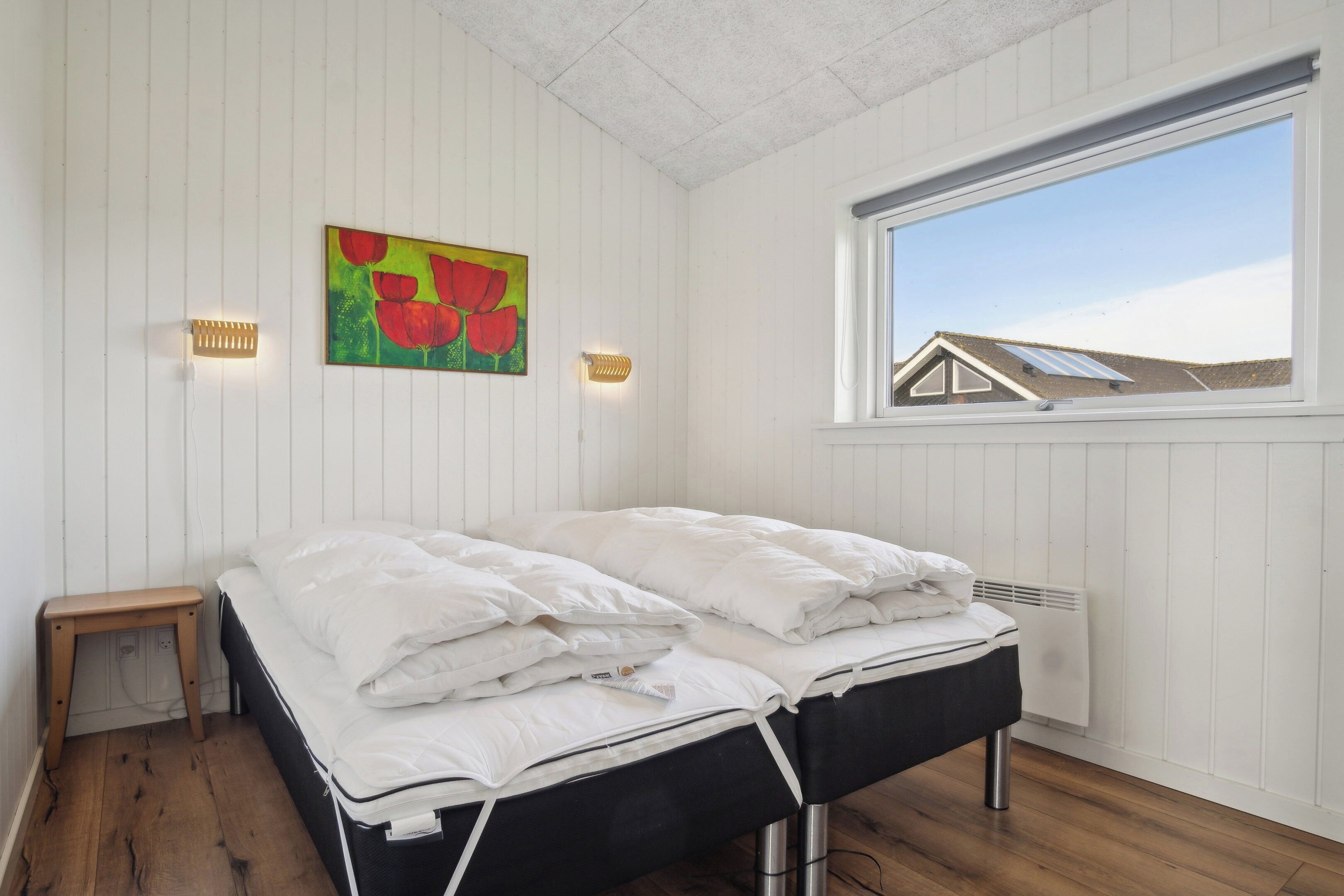 A bedroom with a bed, a window, a radiator, and a painting on the wall.