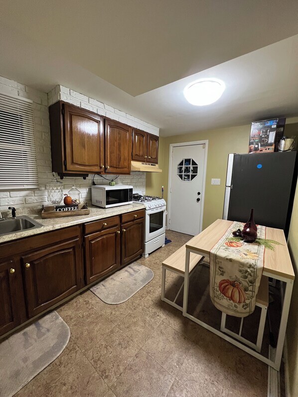 A kitchen with wooden cabinets, a microwave, stove, refrigerator, and a table with a tablecloth.