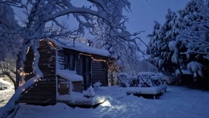 Une cabane enneigée avec un porche, illuminée par des guirlandes lumineuses.