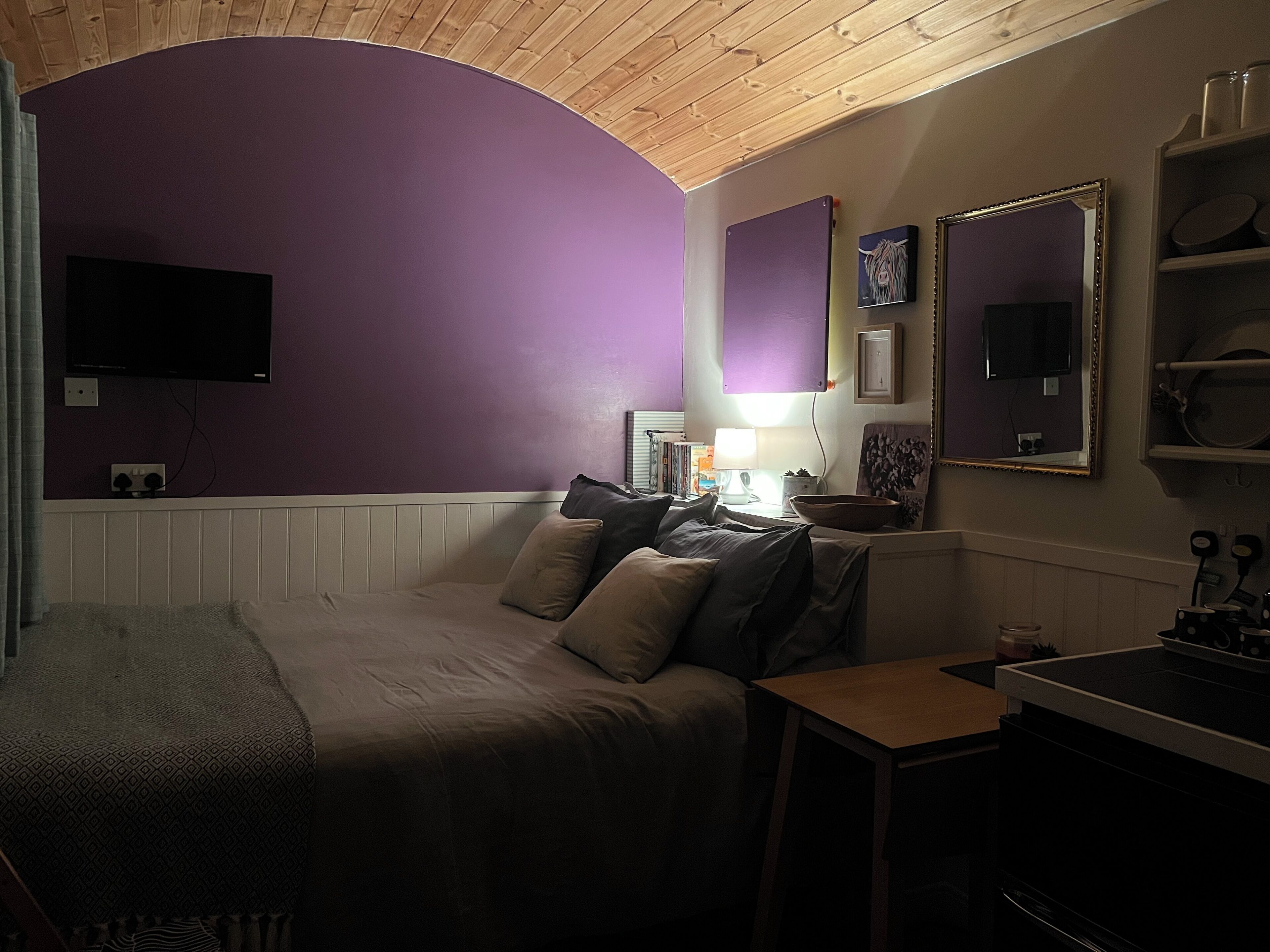 A bedroom with a bed, a desk, and a TV mounted on the wall.