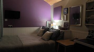 A bedroom with a bed, a desk, and a TV mounted on the wall.