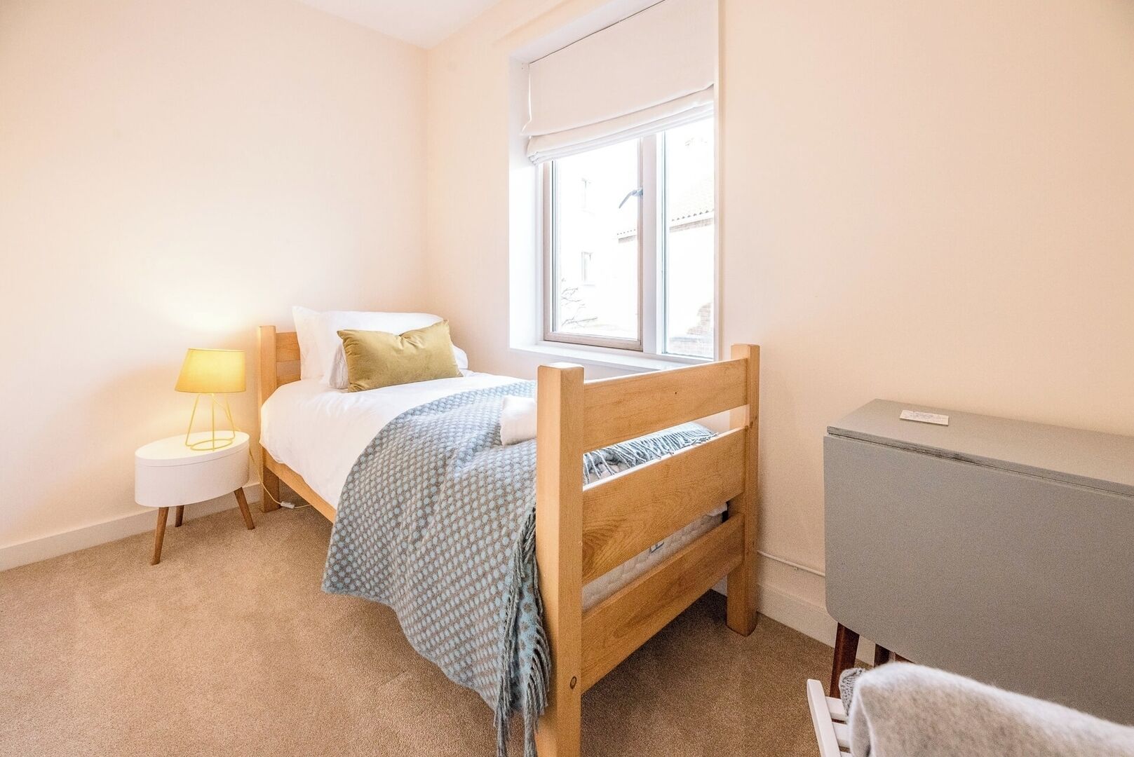 A bedroom with a bed, bedside lamp, window, and a small cabinet.