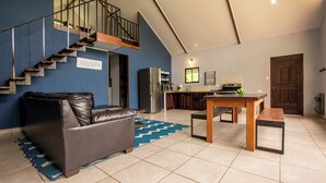 A modern living room with a leather sofa, a dining table, and a kitchen area with appliances. - Casa Sloth, enchanting private house near La Fortuna. (Provincia de Alajuela)