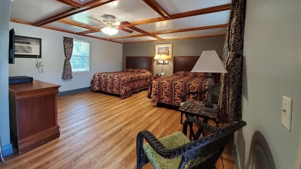 A room with a wooden ceiling, two beds with patterned bedding, a desk, and a chair. - High Springs Country Inn (High Springs)