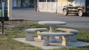 A stone outdoor seating area with a table and benches, a trash bin, and a building in the background. - High Springs Country Inn (High Springs)