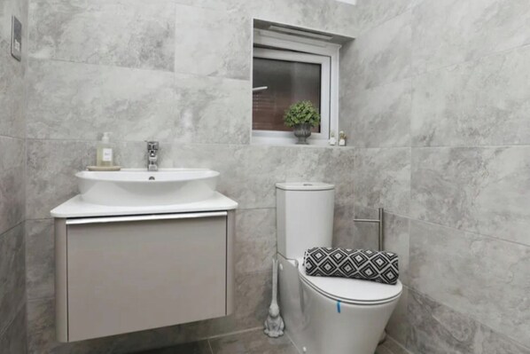 A bathroom with a white sink, toilet, and a window above the toilet.