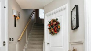 Un escalier menant à une porte ornée d’une guirlande de fleurs et à laquelle est fixée une horloge au mur.