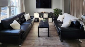 Een woonkamer met twee zwarte leren banken, een salontafel, een flatscreen-tv aan de muur en een bijzettafeltje met decoratieve objecten.