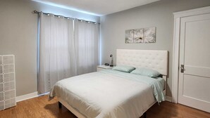 Een slaapkamer met een bed, nachtkastje, een kunstwerk aan de muur en een deur.
