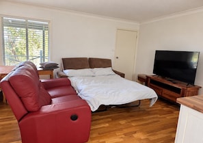 A bedroom with a bed, a red chair, a television, and a wooden floor.