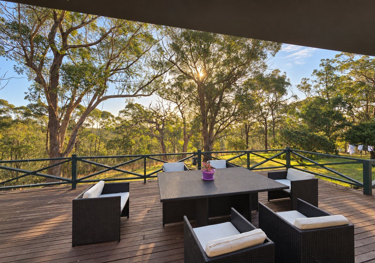 An outdoor deck with a table and chairs, surrounded by a railing and trees.