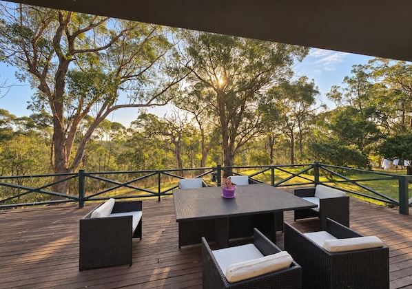 An outdoor deck with a table and chairs, surrounded by a railing and trees.