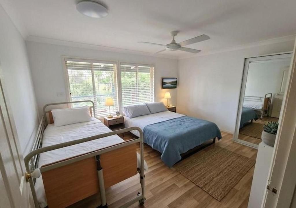 A bedroom with two beds, a ceiling fan, a bedside table with a lamp, and a window with blinds.