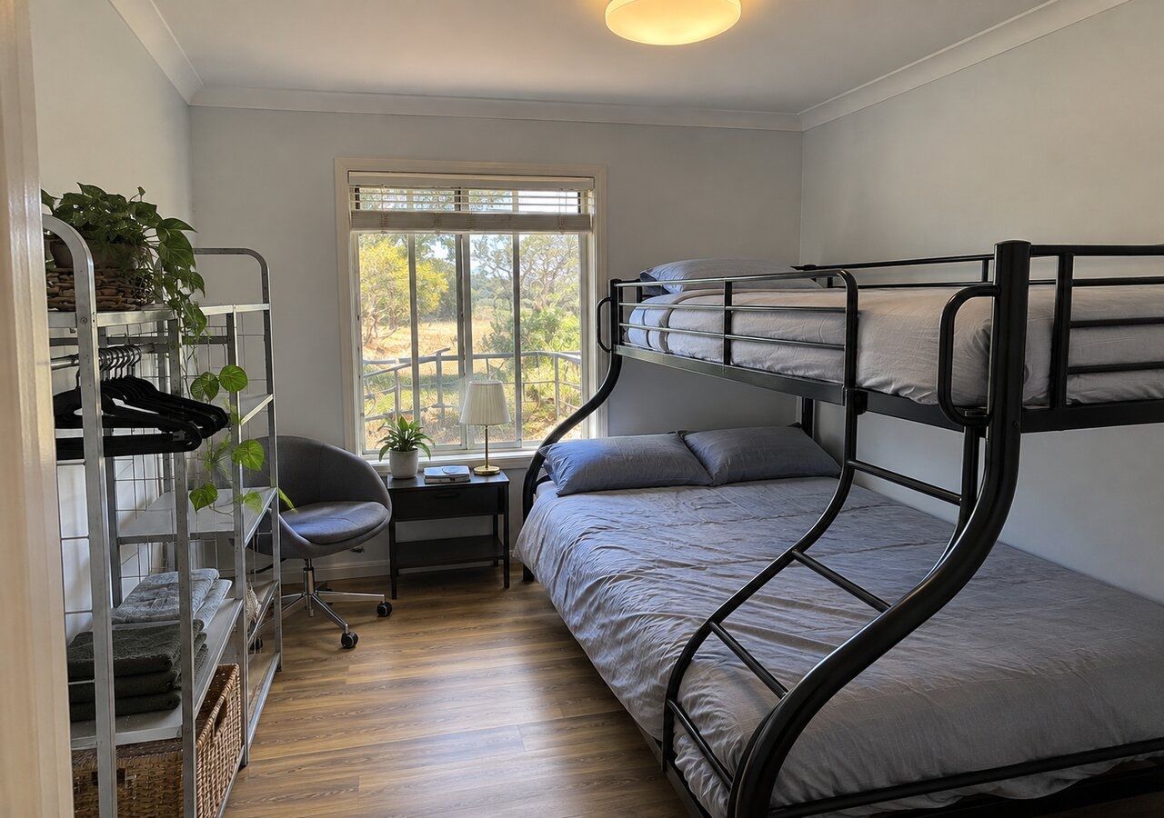 Ein Schlafsaalzimmer mit Etagenbetten, einem Schreibtisch, Stuhl und einem Fenster mit Blick auf Bäume.