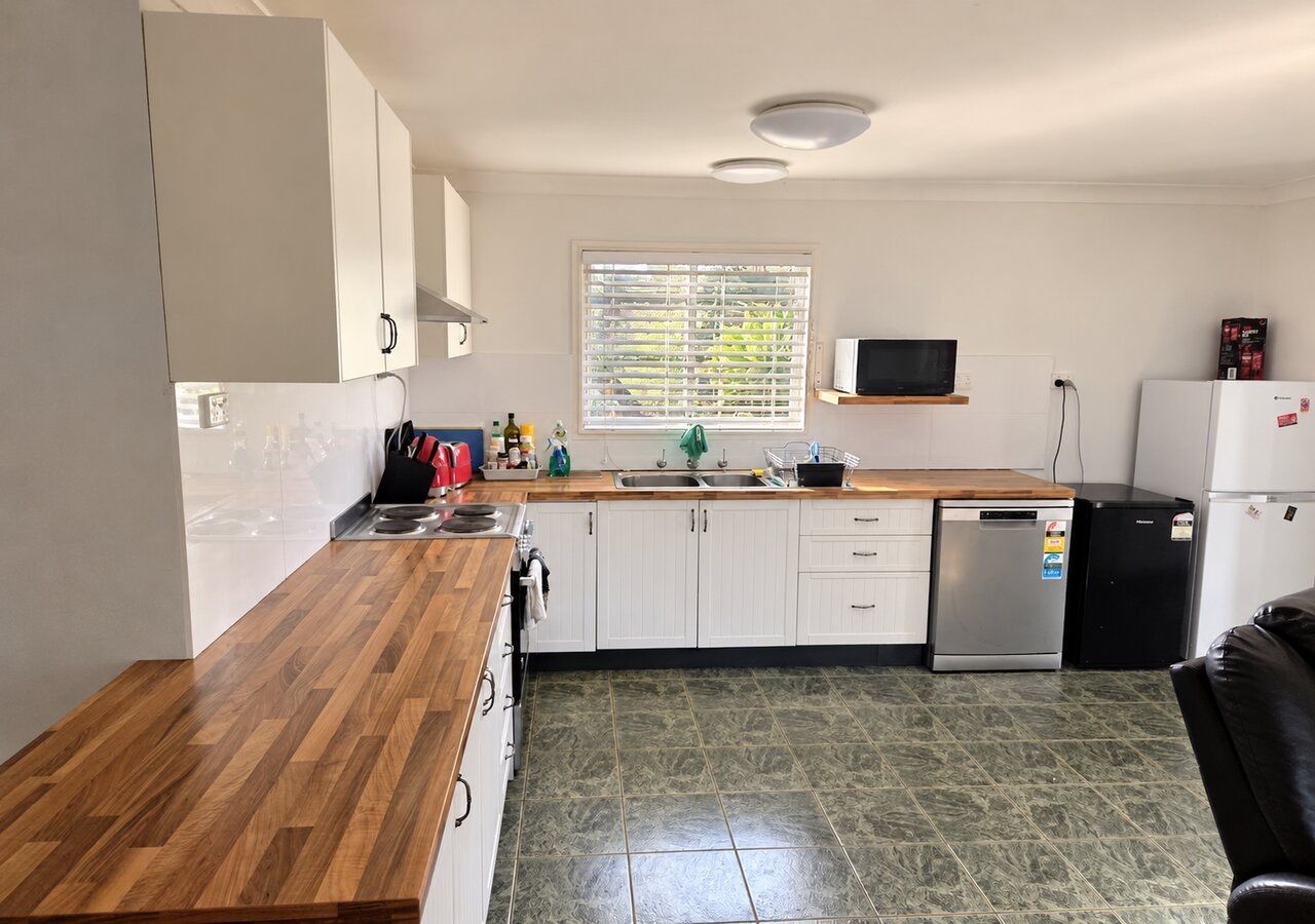 A kitchen with white cabinets, a wooden countertop, a stainless steel dishwasher, and a black refrigerator.