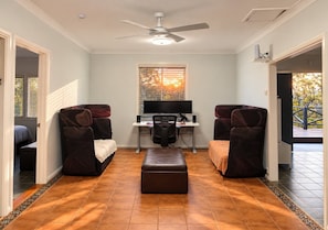 A room with a desk, two chairs, a television, and a ceiling fan.