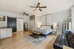 A modern, well-lit room with a bed, a sofa, a dining area, and a kitchen.