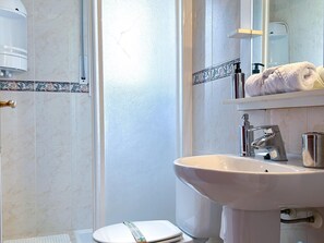 Baño con lavamanos blanco, inodoro y zona de ducha.