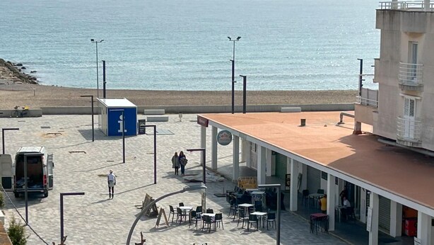 Een kustgebied met een strand, een gebouw met terras en een busje geparkeerd op de stoep.
