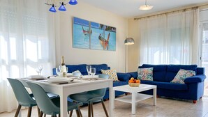 Een moderne woonkamer met een eethoek, met een blauwe bank, een witte salontafel en een eettafel gedekt voor twee personen.