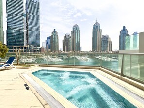 A rooftop pool with a cityscape view, including high-rise buildings and a marina with boats. - 1BR Apt in Prime Location w/ Marina View Balcony (Dubai)
