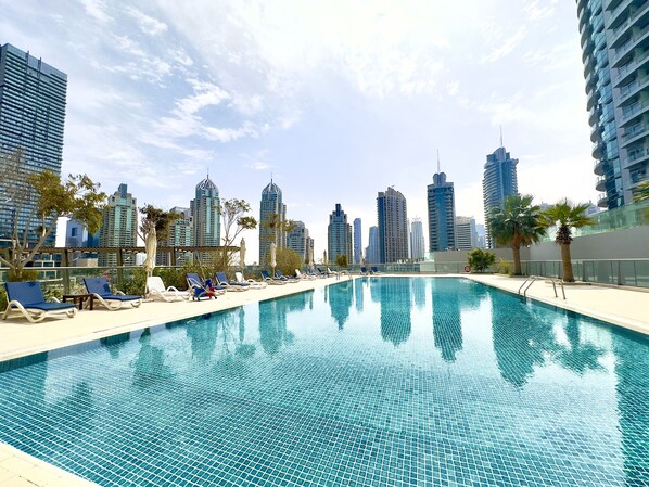 A rooftop pool with lounge chairs and palm trees, surrounded by high-rise buildings.