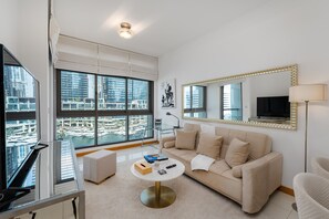 A modern living room with a large window, a sofa, a coffee table, and a TV. - 1BR Apt in Prime Location w/ Marina View Balcony (Dubai)