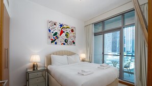 A hotel room with a large bed, two bedside lamps, a decorative wall piece, and a balcony with a view of tall buildings. - 1BR Apt in Prime Location w/ Marina View Balcony (Dubai)
