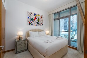 A hotel room with a large bed, two bedside lamps, a decorative wall piece, and a balcony with a view of tall buildings. - 1BR Apt in Prime Location w/ Marina View Balcony (Dubai)
