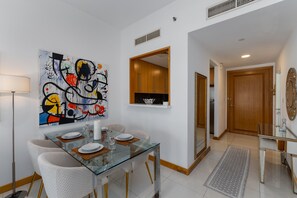 A modern dining area with a glass table, white chairs, and a colorful abstract painting on the wall. - 1BR Apt in Prime Location w/ Marina View Balcony (Dubai)