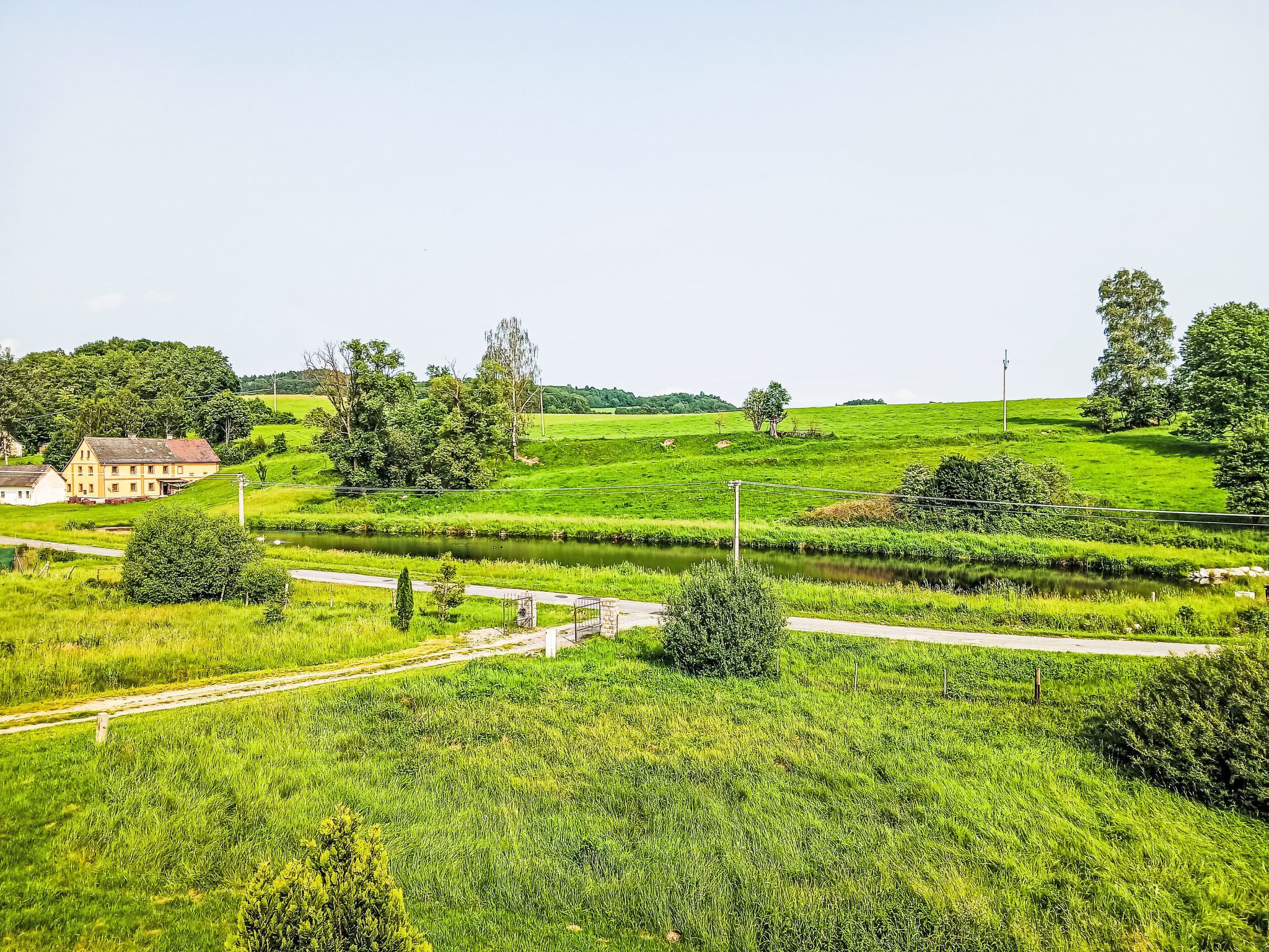 A rural landscape with a house, fields, and a small water body.
